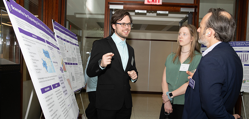 grad student talking to business people about his work in front of a poster