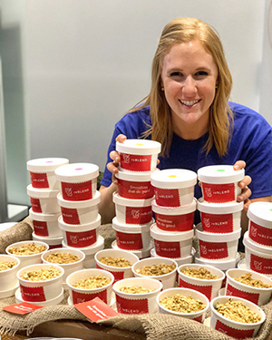 a person smiling while sitting at a table of cups filled with oats