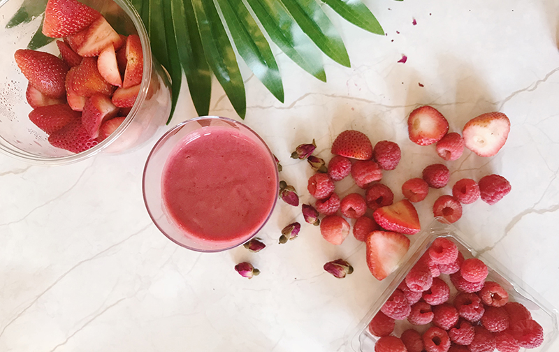 a table full of bright red ingredients (berries, strawberries, etc...) and a bright red smoothie in the center